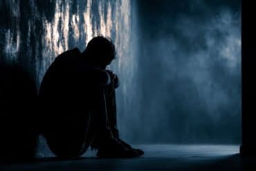 This shows a man sitting against a wall, alone.